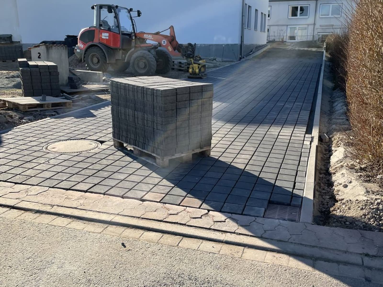 Palette mit Betonsteinen auf der halb fertigen Pflasterfläche, daneben Rinne und Randeinfassung